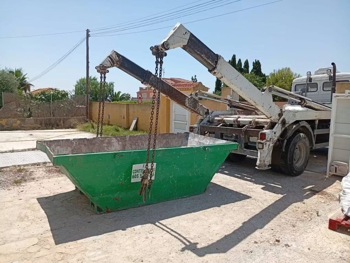 Benne verte de l'entreprise prête à être posée, accrochée au bras du camion