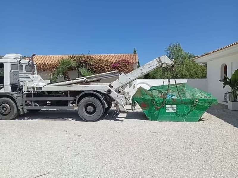 Camion déposant une benne verte bâchée devant une maison individuelle