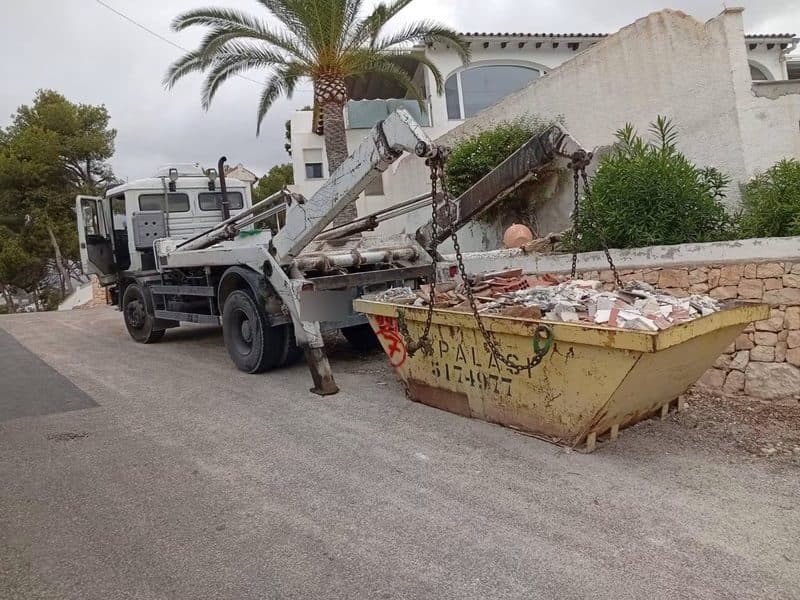 Benne remplie de gravats et de carrelage chargée sur un camion porte-benne