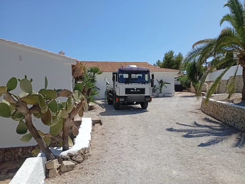 Camion porte-benne manœuvrant dans l'allée étroite d'une maison individuelle