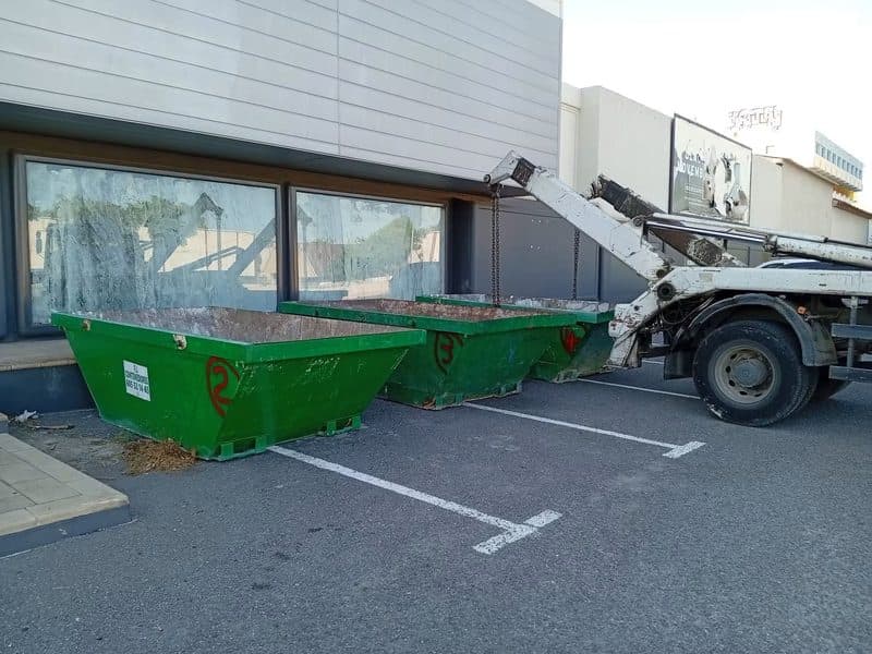 Trois bennes vertes alignées devant un local commercial en cours de curage