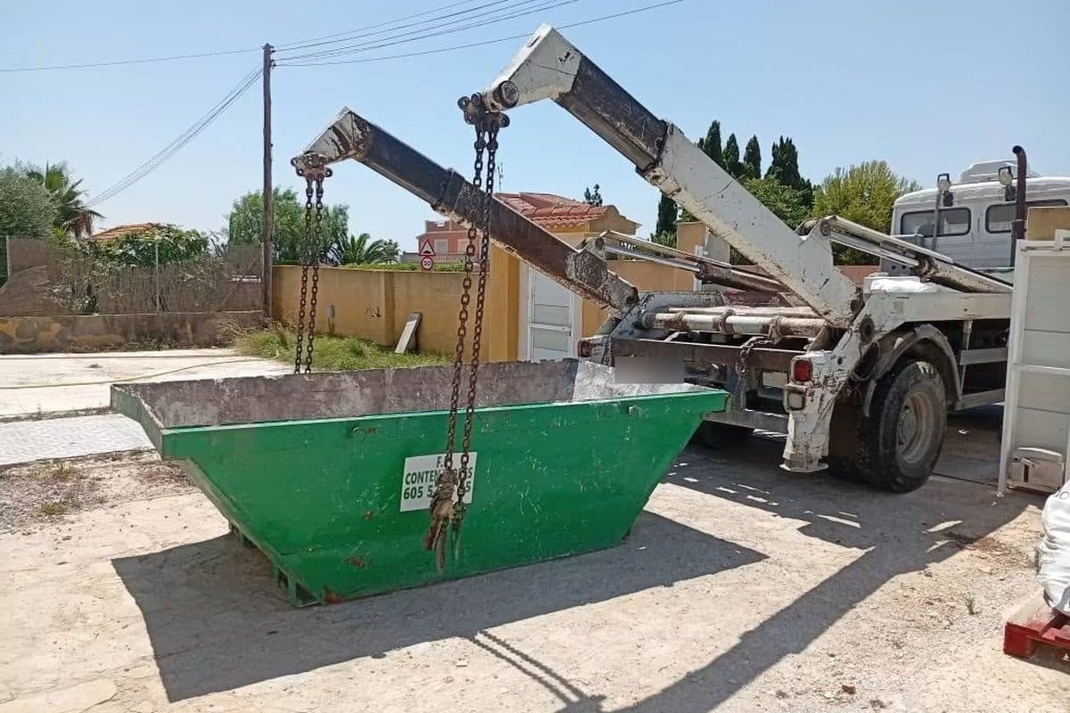 Camion porte-benne de l'entreprise posant des bennes devant un local commercial