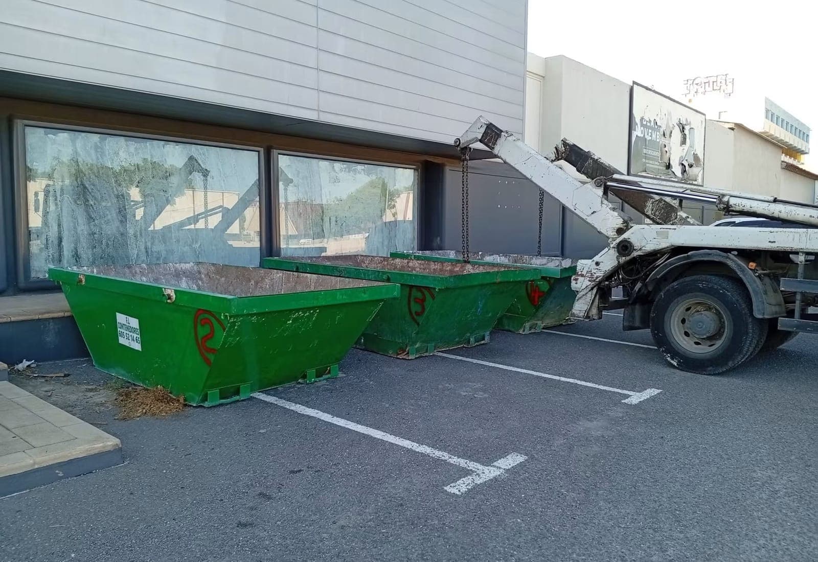 Les bennes de l'entreprise alignées, avec le camion porte-benne en approche