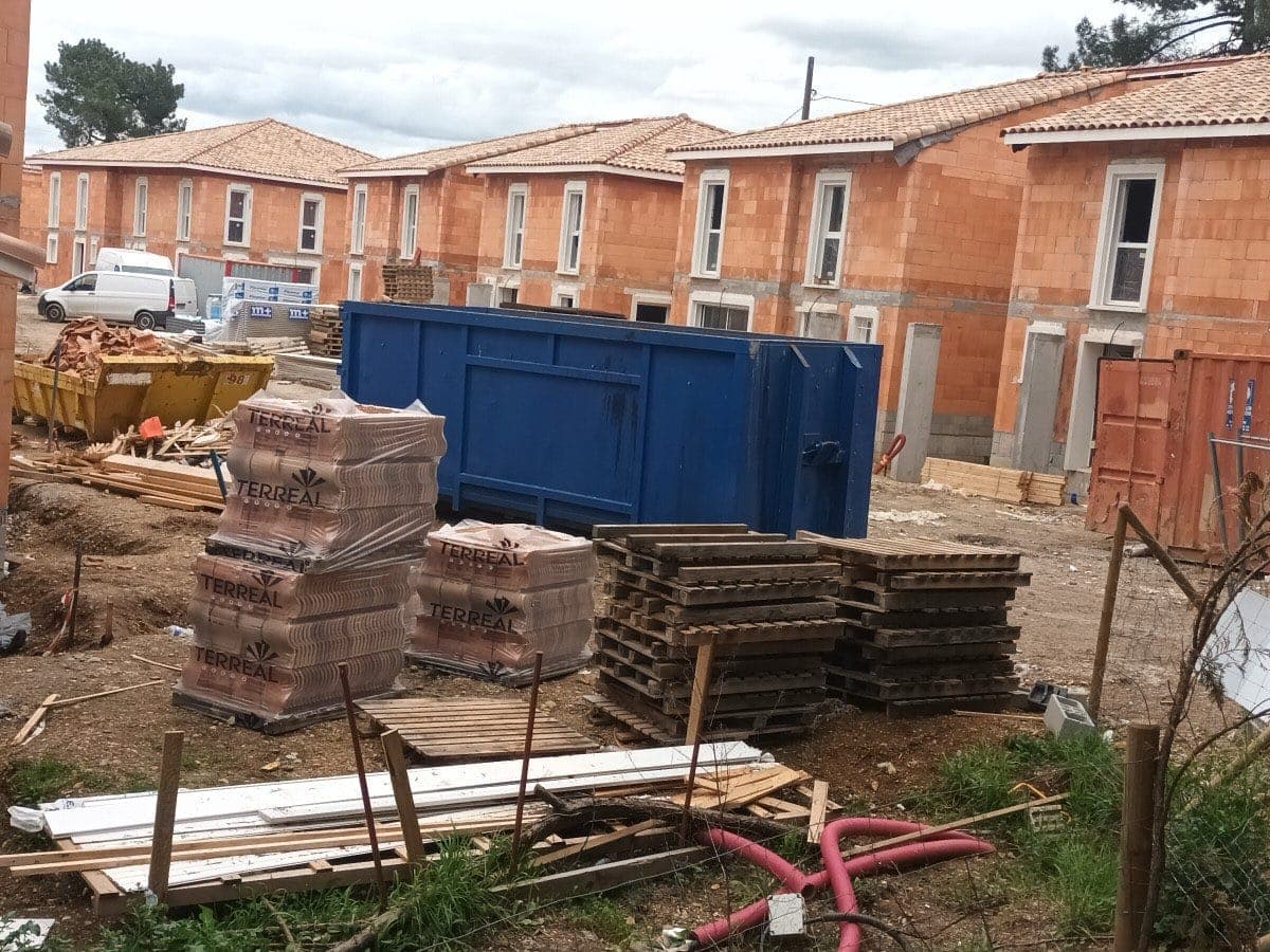 Benne de grand volume posée au milieu d'un lotissement de maisons en construction