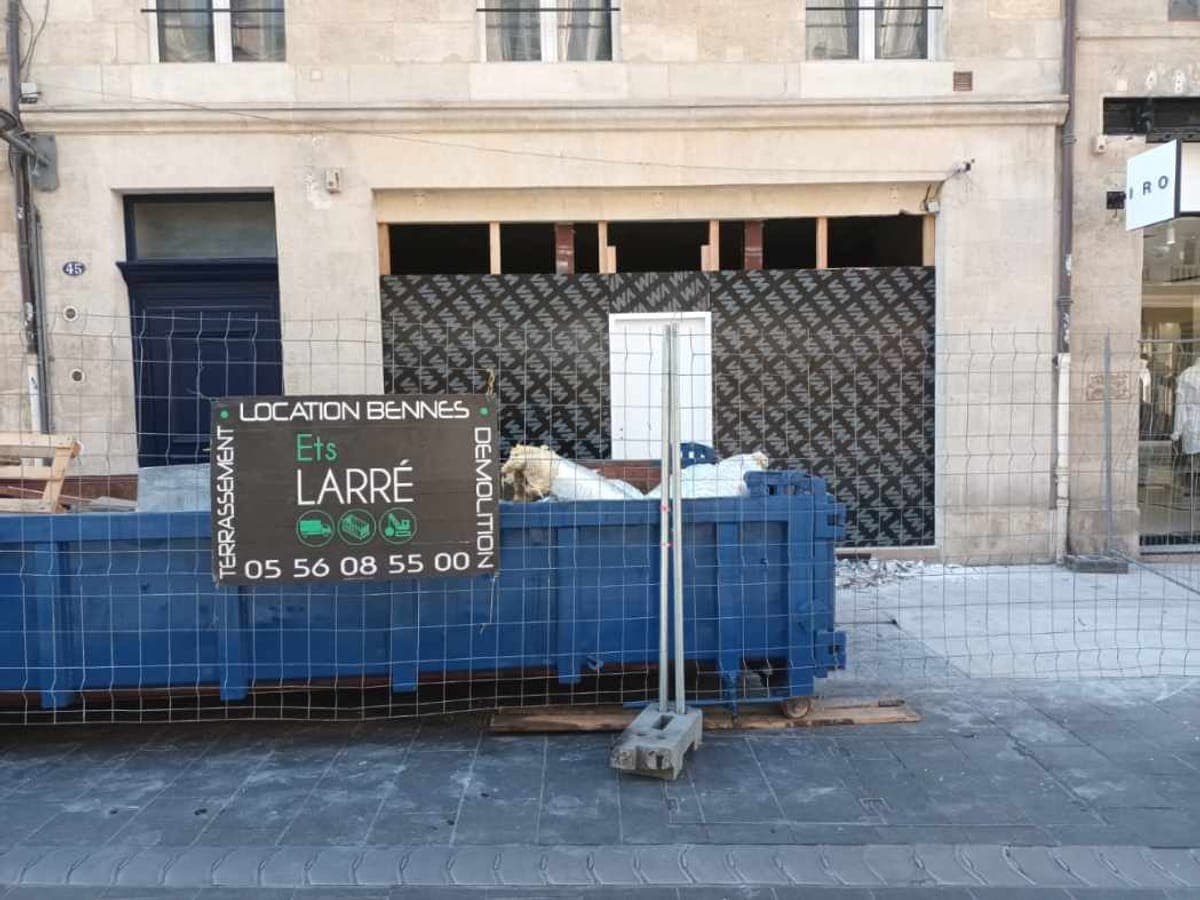 Benne posée devant une boutique en cours de curage, chantier protégé en rue commerçante
